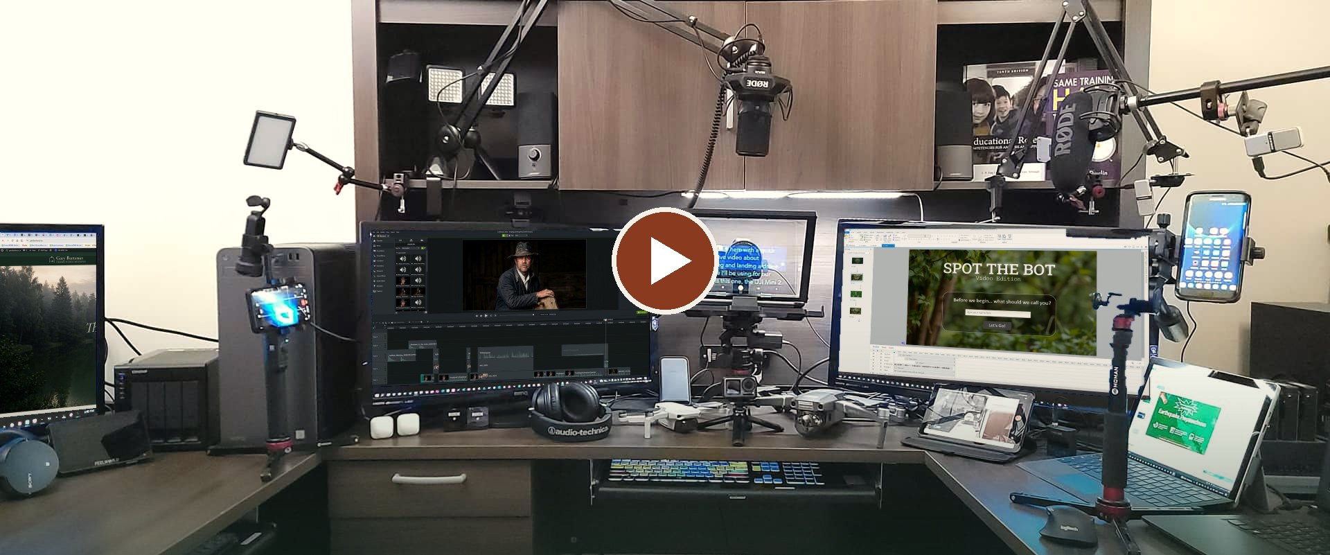 Gary Bartanus's home studio: four monitors showing his course and video work, studio microphones on boom arms, LED panel lights, a teleprompter, cameras on stabilizers and two drones on the desk. Select to watch the 2-minute showreel.